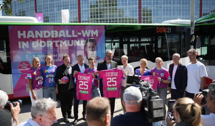 Gruppe posiert vor Westfalenhalle mit Bus im Handball-WM 25 Branding