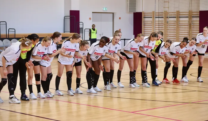 Eine Handball-Frauenmannschaft steht zusammen in einer Halle und lacht. 