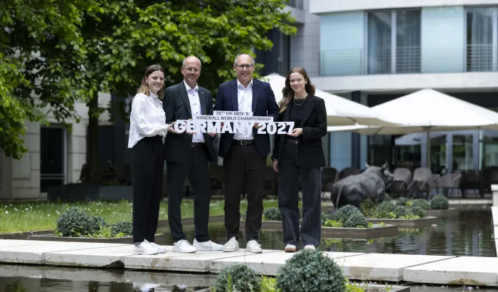 Zwei Männer und zwei Frauen halten vor einem Radisson Hotel den Schriftzug der Handball-Weltmeisterschaft 2027 in die Höhe.