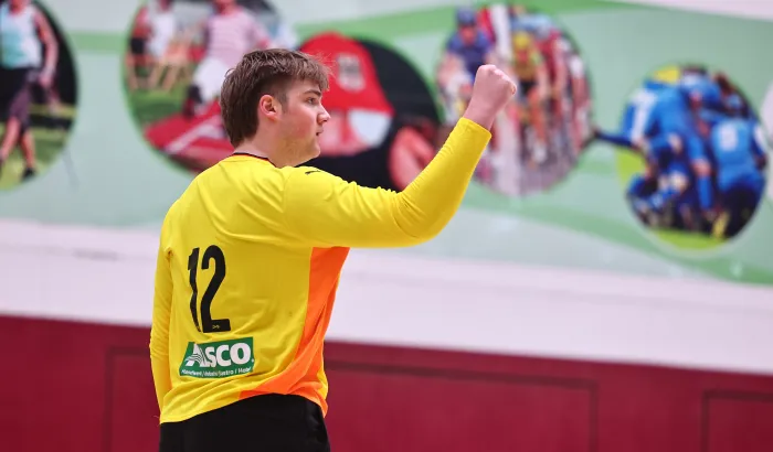 Ein junger Mann in einem orangen Trikot der die Faust ballt und sich freut. 