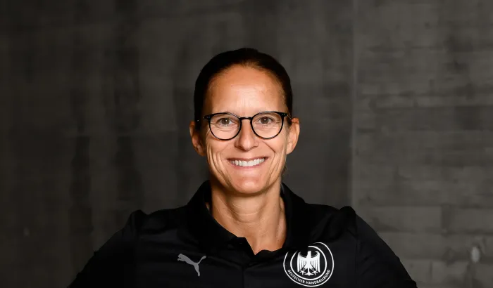 Eine Frau in einem schwarzen Shirt die lacht und die Arme seitlich aufgestellt hat. 