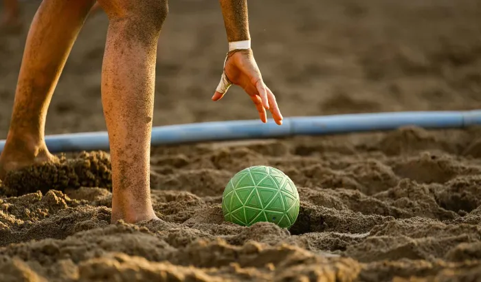Eine Hand hebt den Beachhandball aus dem Sand