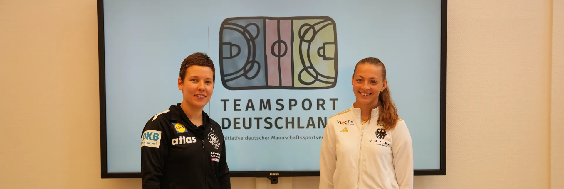 Zwei Spielerinnen vor einem großen Screen stehend. 