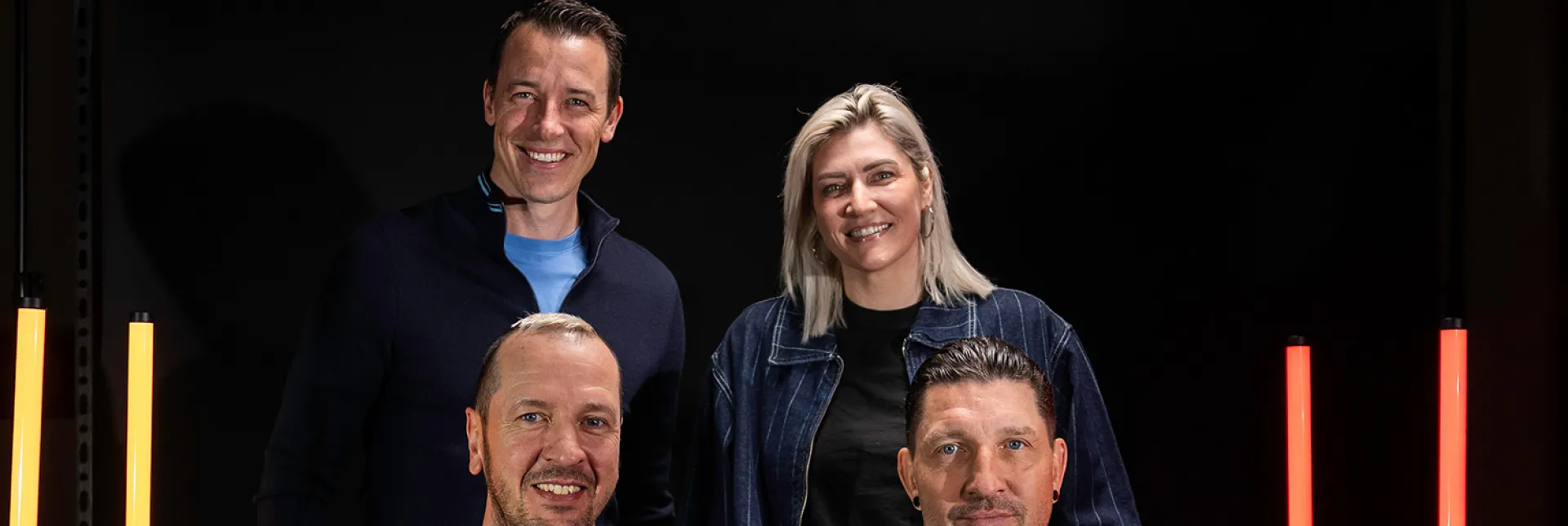 Die 4 WM-Botschafter gemeinsam beim Fotoshooting vor schwarzem Hintergrund mit gelben und roten Lichtsäulen.