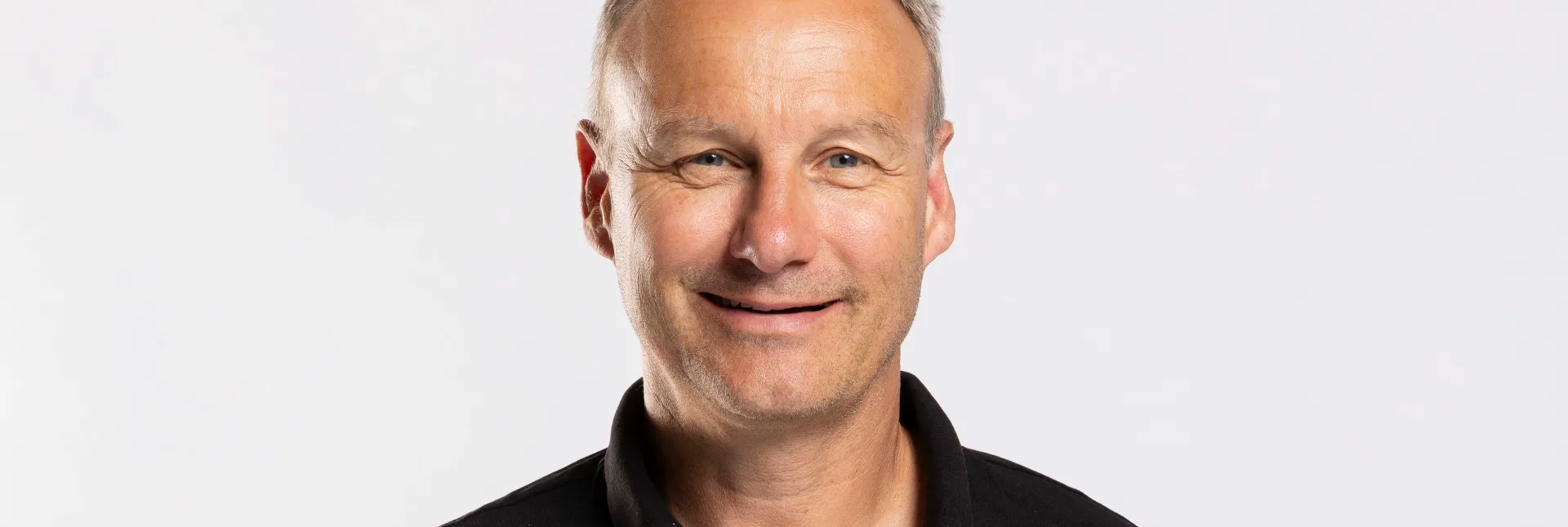 Ein Mann mit verschränkten Armen hinter dem Rücken der in die Kamera lächelt.