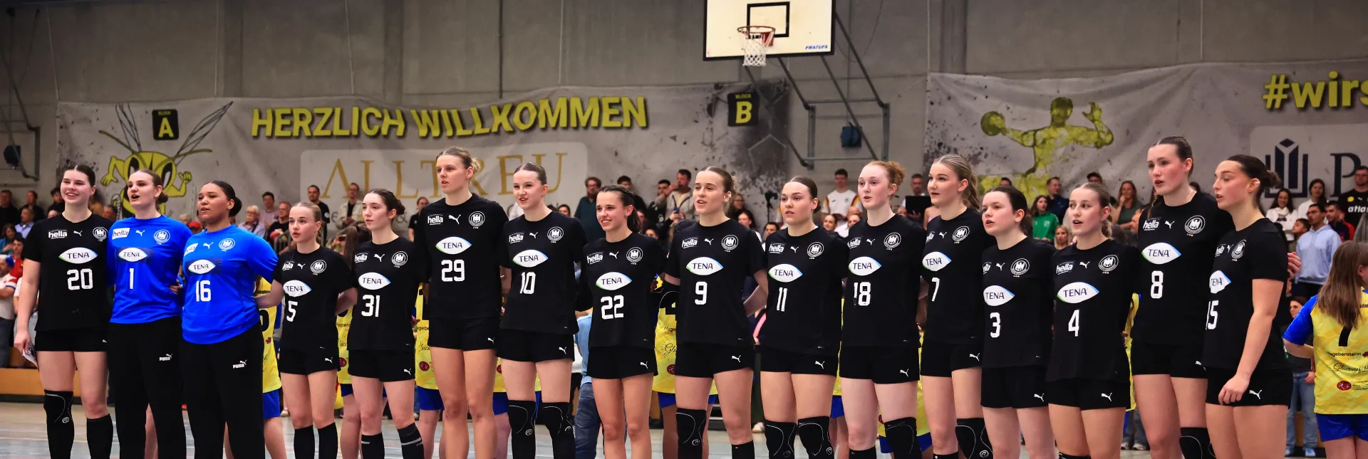 Eine Truppe von Mädels in Hnandballsachen, die zusammenstehen mit den armen ineinander verschlungen.. 