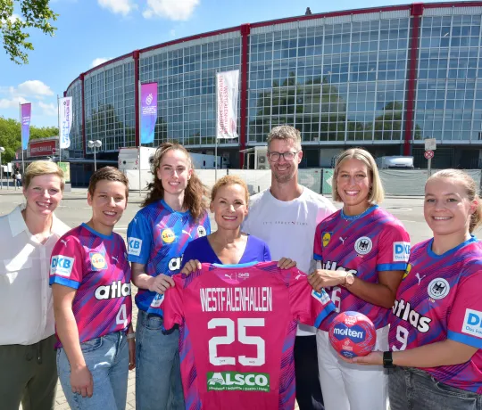 Spielerinnen der Nationalmannschaft, Bundestrainer Markus Gaugisch, Clara Woltering und Sabine Loos posieren vor der Westfalenhalle mit Trikot.