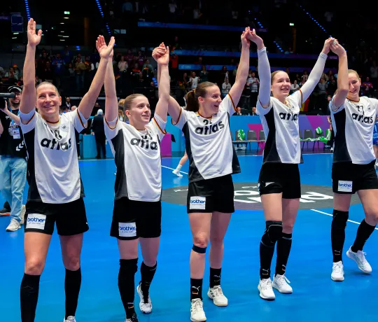 Handballspielerinnen jubeln nach einen Sieg auf dem Feld zu ihren Fans.
