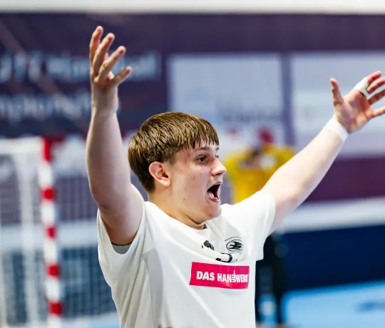 Ein junger Mann in einem weißen Trikot der die Hände in die Luft streckt und schreit. 