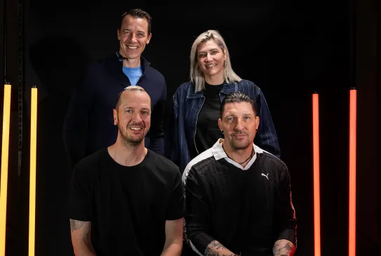 Die 4 WM-Botschafter gemeinsam beim Fotoshooting vor schwarzem Hintergrund mit gelben und roten Lichtsäulen.