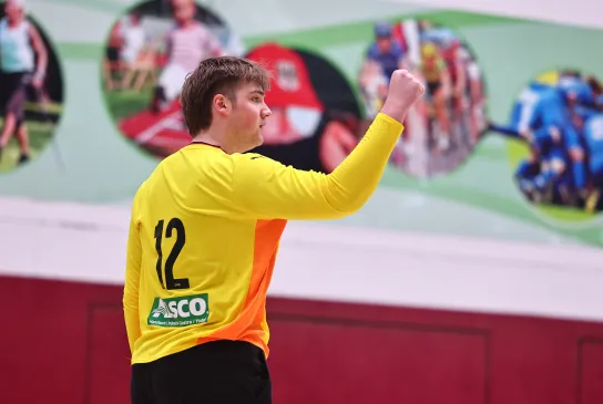 Ein junger Mann in einem orangen Trikot der die Faust ballt und sich freut. 