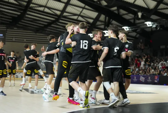 Eine Truppe von Handballerinnen in schwarzen Trikots die bei einem Tor aufstehen und jubeln
