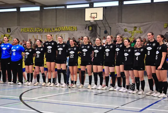 Eine Truppe von Mädels in Hnandballsachen, die zusammenstehen mit den armen ineinander verschlungen.. 