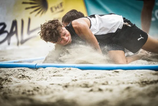 Zwei Spieler kämpfen im Sand um den Ball.