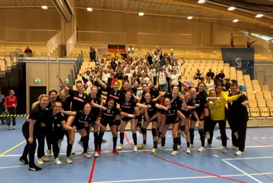 Eine Truppe von Mädels in Hnandballsachen, die zusammenstehen mit den armen ineinander verschlungen.. 